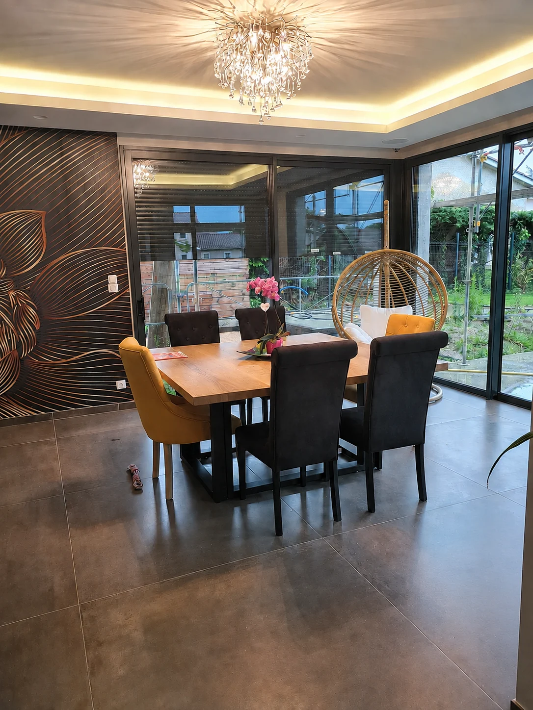 Salle à manger avec plafond à éclairage indirect, lustre et papier peint à motifs dorés.